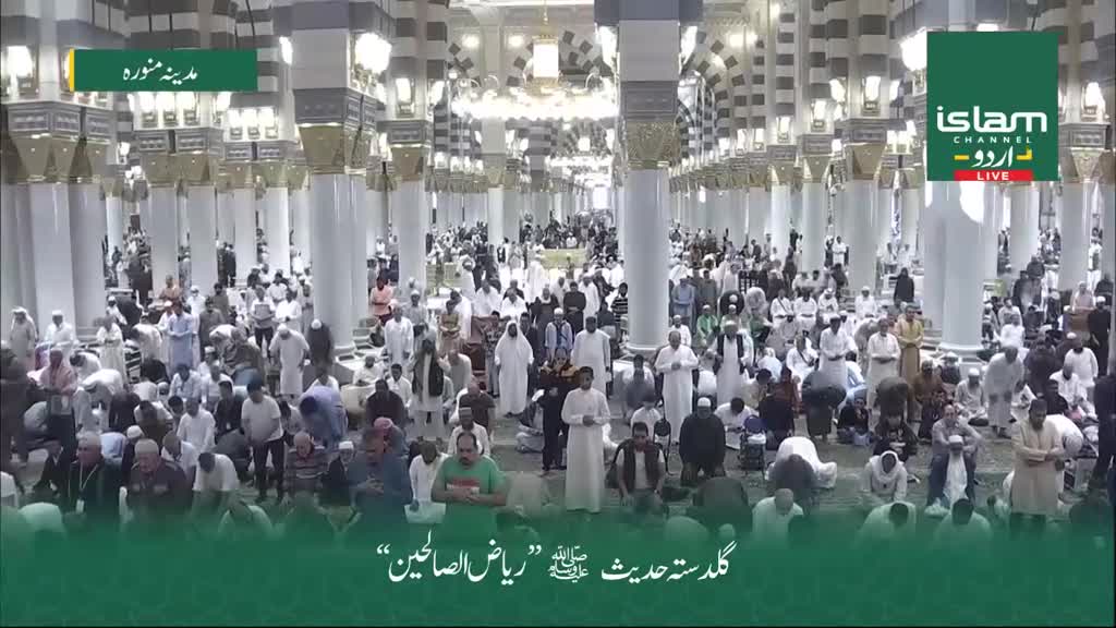 People are gathered in a vast hall, many kneeling or bowing in prayer. The scene is being broadcast live by Islam Channel Urdu, with the words "Madinah Munawwarah" displayed on screen.
