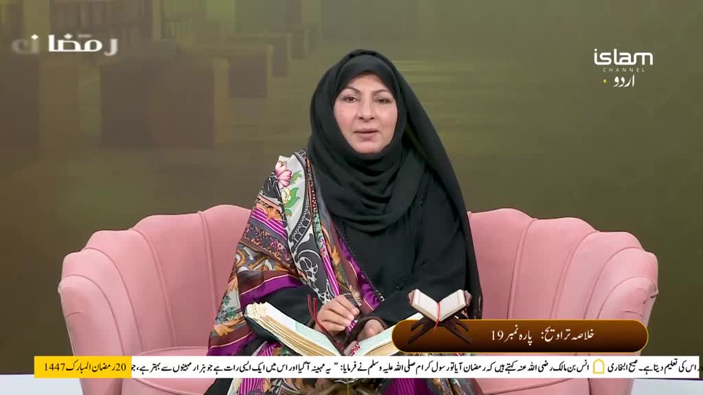 A woman in a black hijab and a colourful shawl speaks from a plush pink chair. She gestures towards an open book on her lap, its pages filled with Urdu script. A woman in a black hijab and a colourful shawl speaks from a plush pink chair. She gestures towards an open book on her lap, its pages filled with Urdu script.