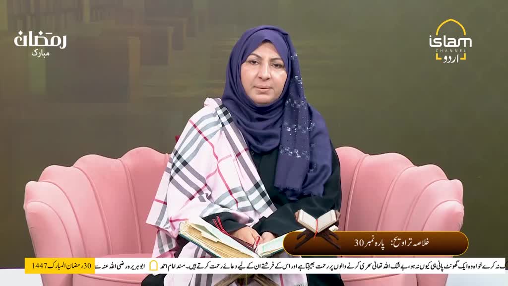 A woman in a hijab sits on a pink sofa, a book open before her. She's wearing a plaid shawl draped over her shoulders as she speaks. A woman in a hijab sits on a pink sofa, a book open before her. She's wearing a plaid shawl draped over her shoulders as she speaks.