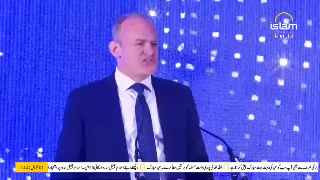 A man in a dark suit and tie speaks at a podium. The Islam Channel Urdu logo appears on the screen behind him. A man in a dark suit and tie speaks at a podium. The Islam Channel Urdu logo appears on the screen behind him.