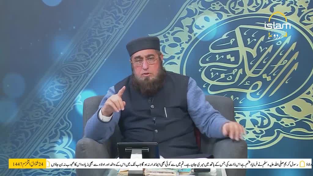 A man with glasses and a beard, wearing a cap and a dark vest over a blue shirt, gestures with his right hand. He sits in a studio with a blue, patterned backdrop featuring Arabic calligraphy and the Islam Channel Urdu logo.