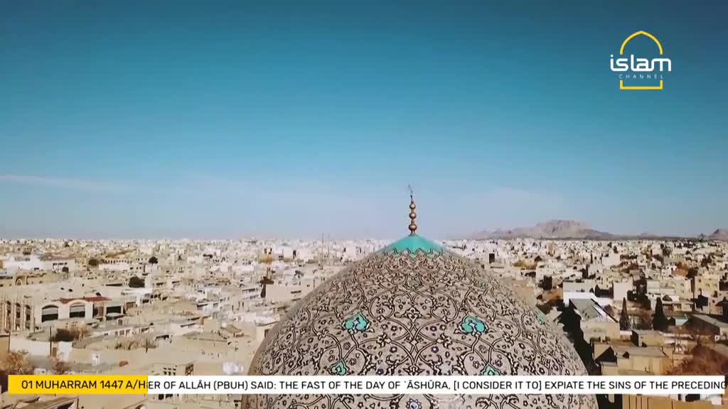 The camera hovers above a patterned dome, its turquoise top pointing toward a bright blue sky. Below, a sprawling city spreads out, with a mountain range visible in the distance.
