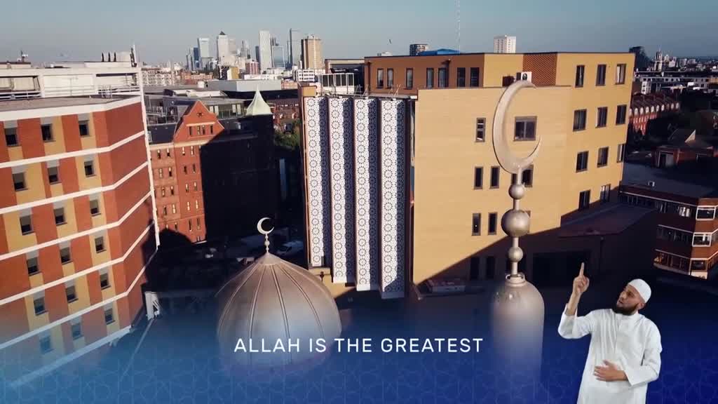A man in a white robe gestures upward near a mosque's minaret, the crescent moon atop it gleaming in the sunlight. The cityscape of the United Kingdom forms a backdrop, with text from the Islam Channel, "Allah is the Greatest," appearing below.

