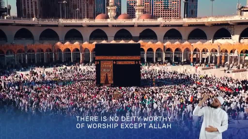 A sea of people in white surrounds the Kaaba, a black cube-shaped structure. A man in traditional attire raises his hands, as if in prayer, against the backdrop of the sacred mosque.
