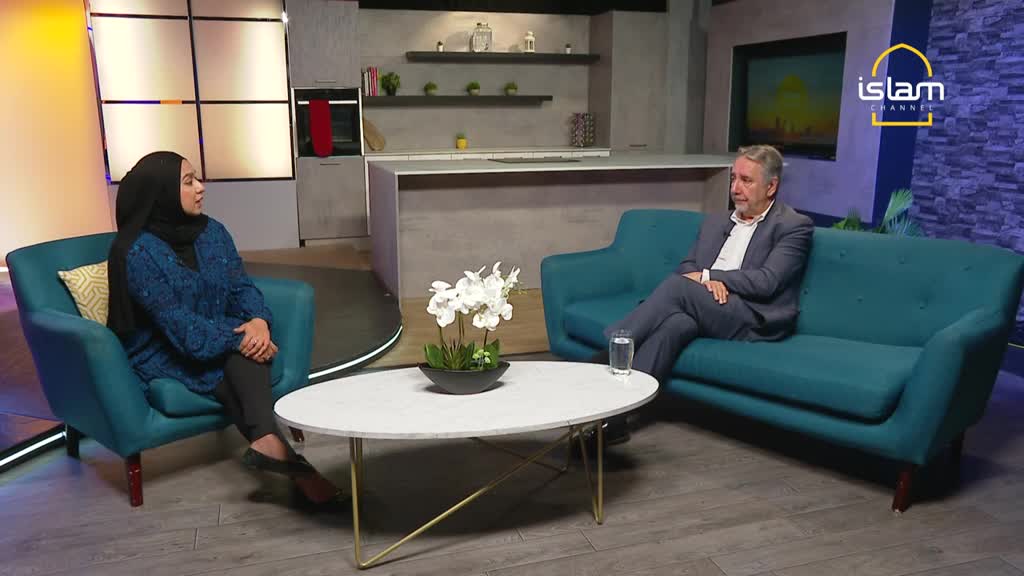 A woman in a hijab sits across from a man on a teal couch, both in a studio set. The Islam Channel logo is visible, and a glass of water rests on the coffee table between them.
