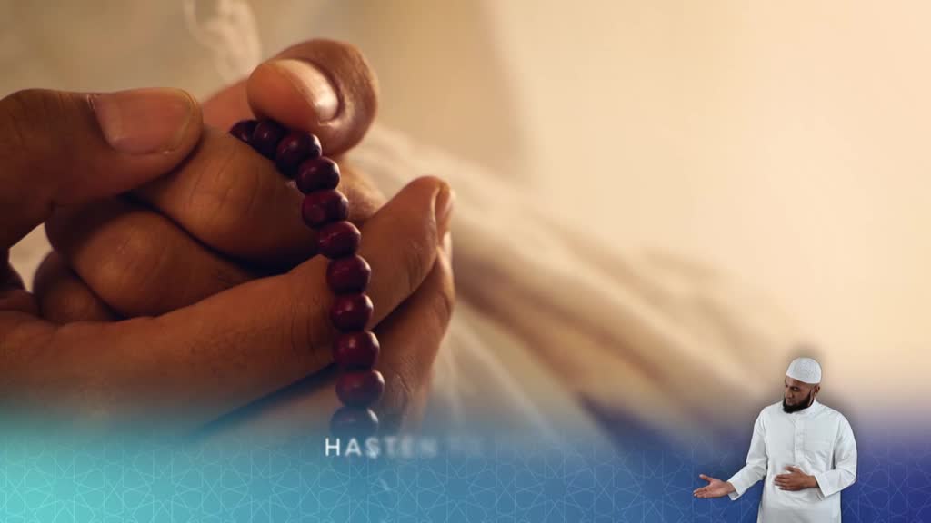 A hand, holding a string of dark beads, gently moves them between the fingers. Beside it, a man in a white robe gestures toward the viewer, likely on a program from the United Kingdom's Islam Channel.
