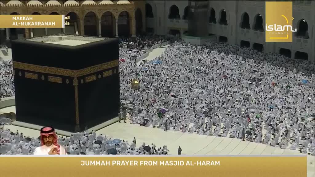 The Kaaba stands in the center, a dark cube surrounded by a sea of white-clad figures. The crowd is gathered, likely for prayer, with the scene broadcast live on the Islam Channel.
