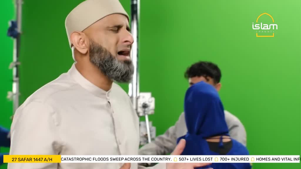 A man in a white shirt and cap is speaking, his face etched with emotion, while a person in a blue hijab stands nearby. Behind them, a green screen provides a backdrop for what appears to be a broadcast on the Islam Channel.
