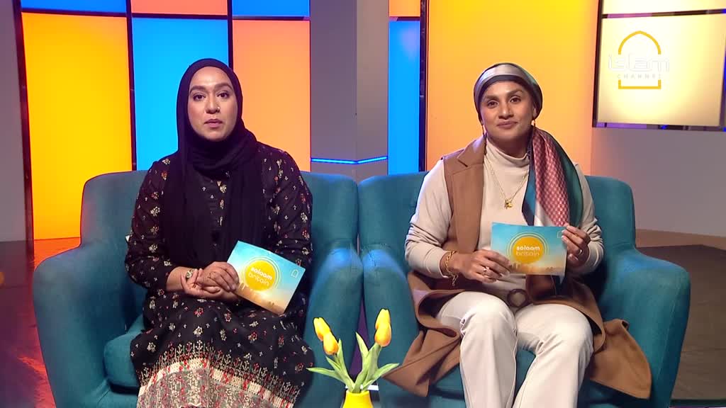 Two women sit on matching teal chairs, each holding a small card with a sunrise design. They're in a studio setting, presumably for a program on the Islam Channel, with a colorful backdrop behind them.
