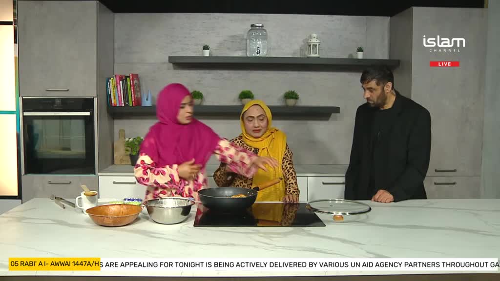 On the Islam Channel set, a woman in a pink hijab gestures towards a pan on the stove. Another woman, wearing a yellow headscarf, is holding a wooden spoon over the pan, while a man in a black jacket observes.
