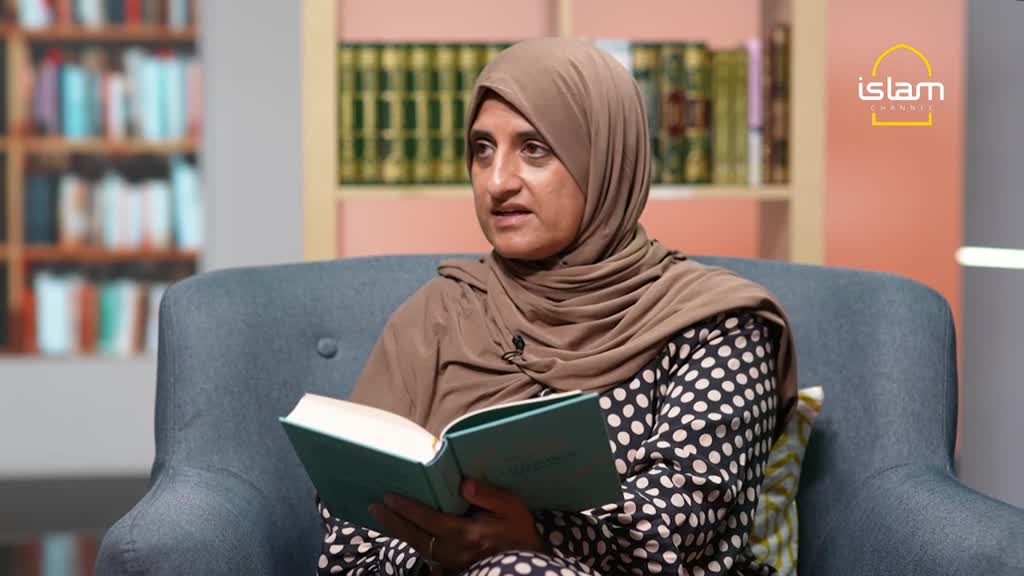 A woman in a brown hijab sits in a chair, holding an open book. She's speaking, likely on the Islam Channel, with a bookshelf visible in the background.
