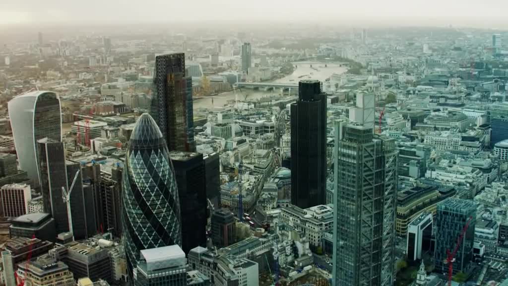 From this high vantage point, the London skyline sprawls out, a dense collection of buildings under a hazy sky. The Gherkin's distinctive shape stands out among the other skyscrapers.
