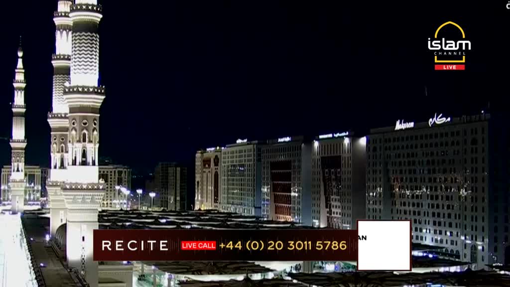 Brightly lit minarets and tall buildings stand under a dark night sky. The Islam Channel logo is visible, with a phone number for live calls from the United Kingdom.
Brightly lit minarets and tall buildings stand under a dark night sky. The Islam Channel logo is visible, with a phone number for live calls from the United Kingdom.