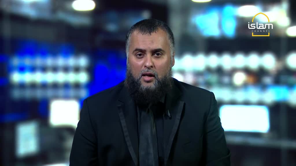 A man with a full, dark beard is speaking directly to the camera, dressed in a black suit. The "Islam Channel" logo is visible in the upper right corner, with a blurred background of lights behind him.
A man with a full, dark beard is speaking directly to the camera, dressed in a black suit. The "Islam Channel" logo is visible in the upper right corner, with a blurred background of lights behind him.