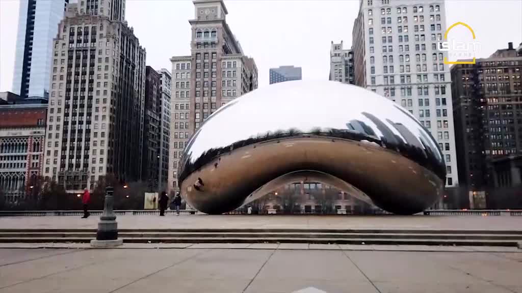 A massive, reflective sculpture sits in front of towering buildings, mirroring the cloudy sky and surrounding architecture. People are strolling around the base of the sculpture, seemingly dwarfed by its size.
A massive, reflective sculpture sits in front of towering buildings, mirroring the cloudy sky and surrounding architecture. People are strolling around the base of the sculpture, seemingly dwarfed by its size.