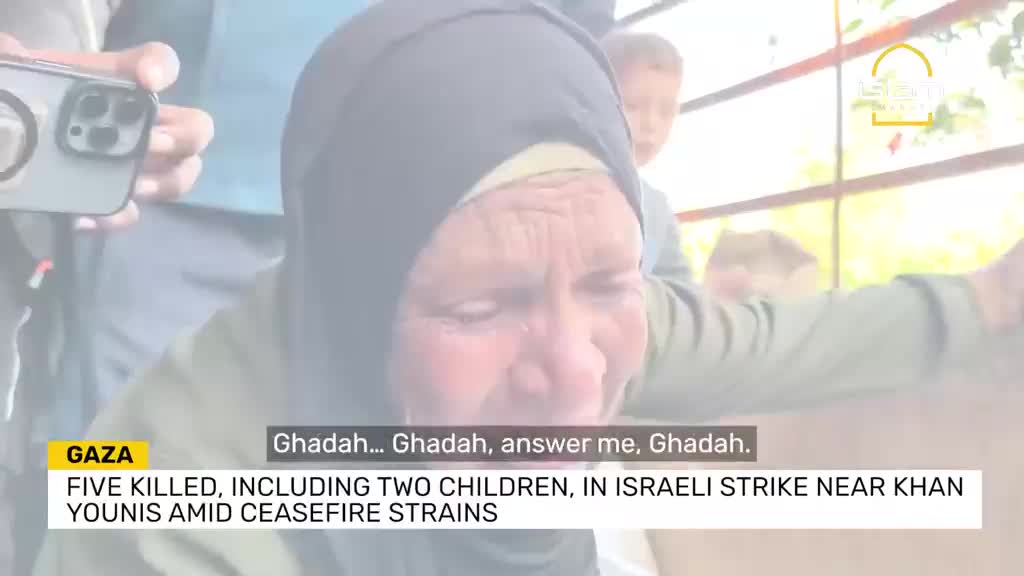 An older woman, her face etched with grief, sobs and calls out a name. The scene is being filmed, the camera held by someone just out of frame.
