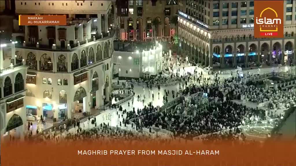 A vast crowd gathers for Maghrib prayer at Masjid Al-Haram in Makkah Al-Mukarramah. People are moving in orderly lines, their white ihrams stark against the illuminated surroundings.