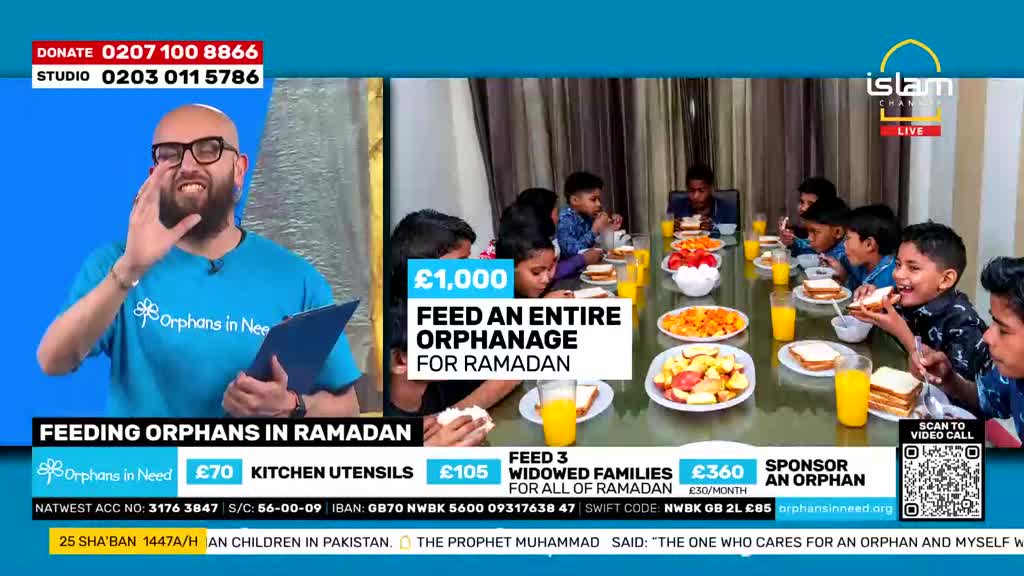 Children are gathered around a long table, eating sandwiches and fruit. A man in a blue shirt with glasses is speaking, gesturing with his hand.