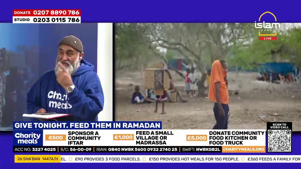 A man in an orange t-shirt walks away, his head covered by the fabric. In the background, several people are gathered under trees.