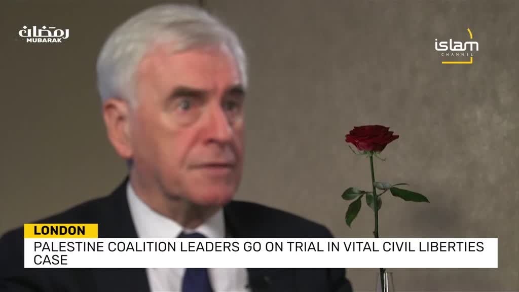 A man in a suit speaks on camera, a single red rose to his right. A graphic at the bottom of the screen announces "LONDON PALESTINE COALITION LEADERS GO ON TRIAL IN VITAL CIVIL LIBERTIES CASE."