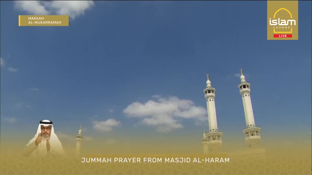A man in traditional attire gives a thumbs-up against a bright blue sky. Towering white minarets rise behind him, their spires reaching towards scattered clouds.