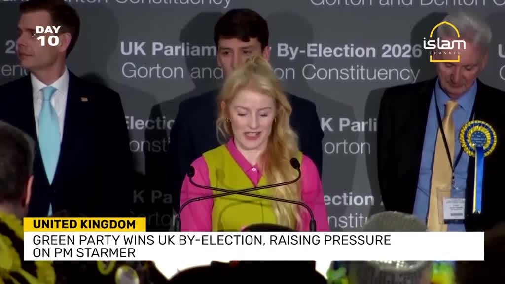 A woman in a bright vest speaks at a podium, while men stand behind her. A banner announces the Green Party's win in a UK by-election.