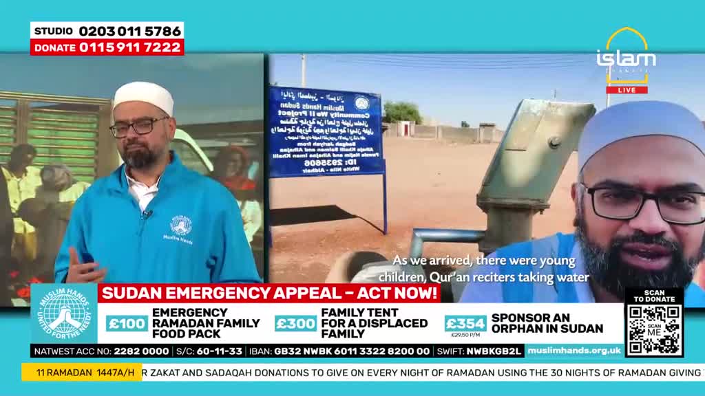 A man in a blue jacket speaks, gesturing with his hands. Behind him, young children are taking water from a pump.