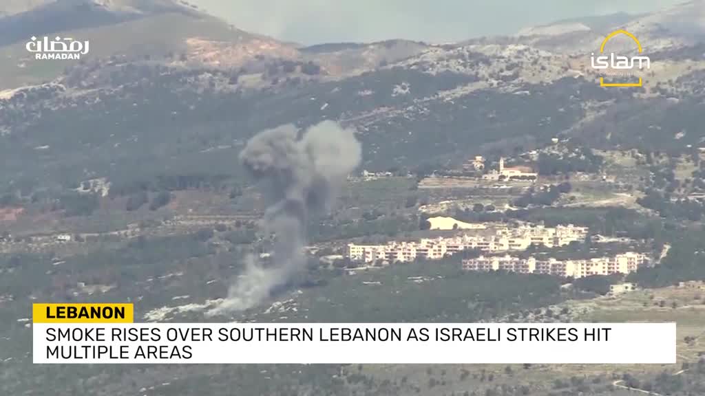 A thick plume of dark smoke billows into the sky over a cluster of buildings. The smoke rises from what looks like a recent impact, spreading out as it ascends.