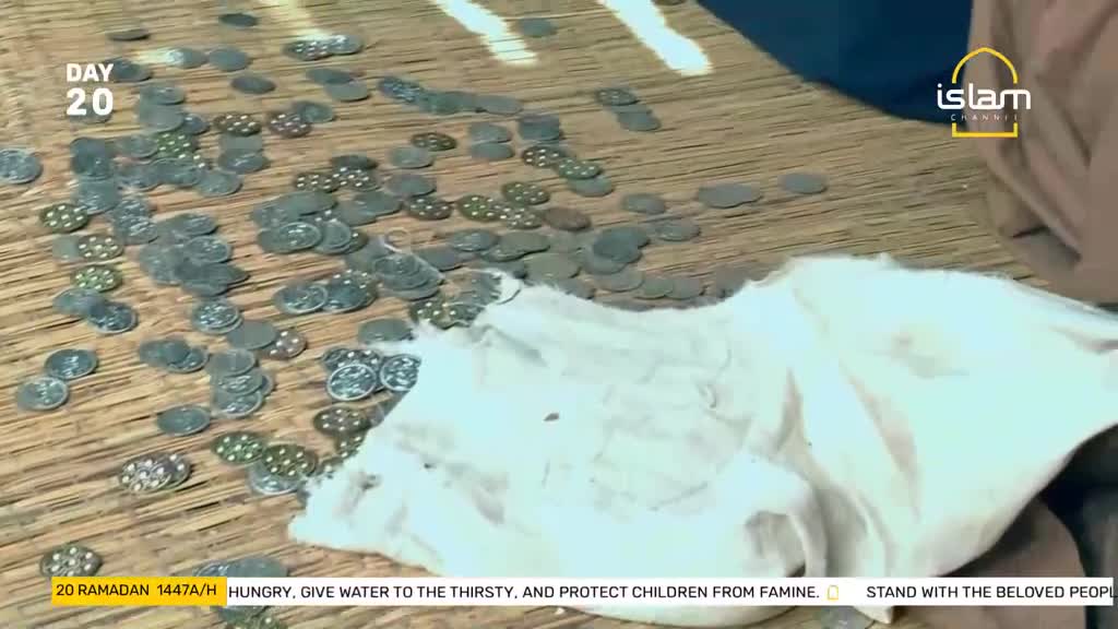 Coins are scattered across a woven mat, some piled, others spread out. A white cloth lies partially covering the coins on the right side of the frame.