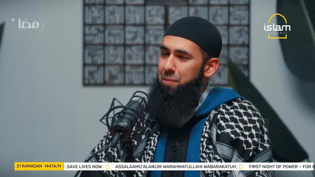 A man with a thick beard and a black kufi is speaking into a microphone. He wears a patterned scarf and a blue hoodie, with the Islam Channel logo visible.
