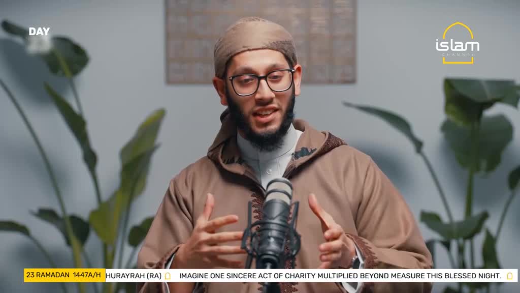 A man in a brown robe and kufi speaks into a microphone, gesturing with his hands. A graphic at the bottom of the screen displays "23 RAMADAN 1447/H HURAYRAH (RA)" and text about charity.