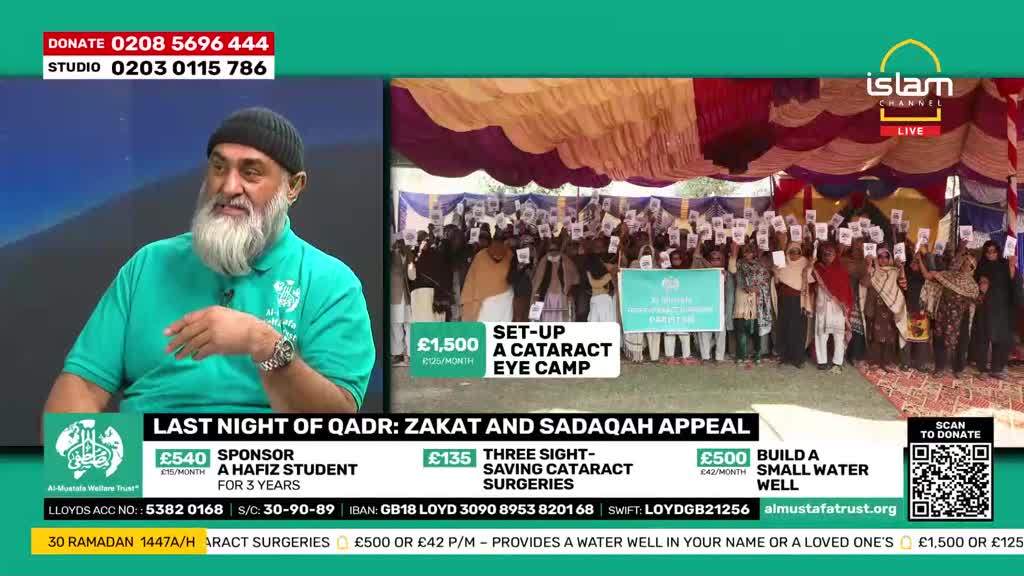 A man with a long grey beard, wearing a green polo shirt and a black beanie, speaks from a studio. Behind him, a large group of people stand under a canopy, holding up papers and a banner. A man with a long grey beard, wearing a green polo shirt and a black beanie, speaks from a studio. Behind him, a large group of people stand under a canopy, holding up papers and a banner.