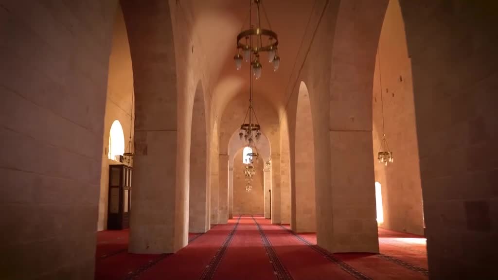 Sunlight streams through arched windows, illuminating a long hall with red carpets. Ornate chandeliers hang from the vaulted ceiling, casting a warm glow. Sunlight streams through arched windows, illuminating a long hall with red carpets. Ornate chandeliers hang from the vaulted ceiling, casting a warm glow.