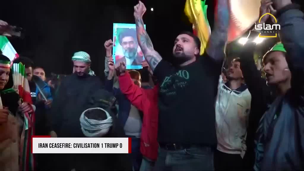 A man with tattoos on his arms raises his fist, holding a portrait of Ayatollah Khomeini aloft. The Islam Channel logo is visible in the background as a crowd cheers. A man with tattoos on his arms raises his fist, holding a portrait of Ayatollah Khomeini aloft. The Islam Channel logo is visible in the background as a crowd cheers.