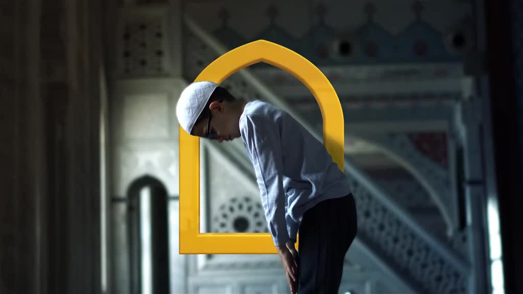 A young man in a white kufi bows his head in prayer. The yellow arch behind him frames his devotional posture within the mosque's interior.