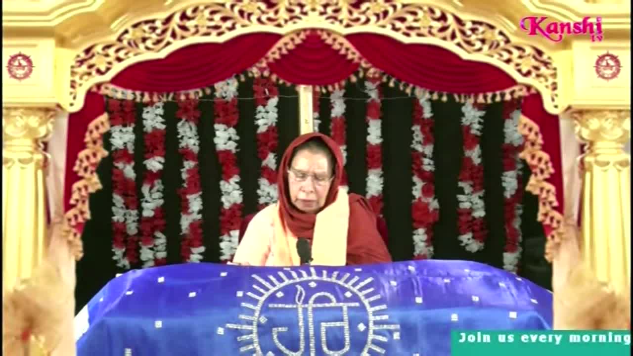 A woman in a headscarf sits behind a blue cloth, speaking into a microphone. The Kanshi TV logo is visible in the top right corner.
