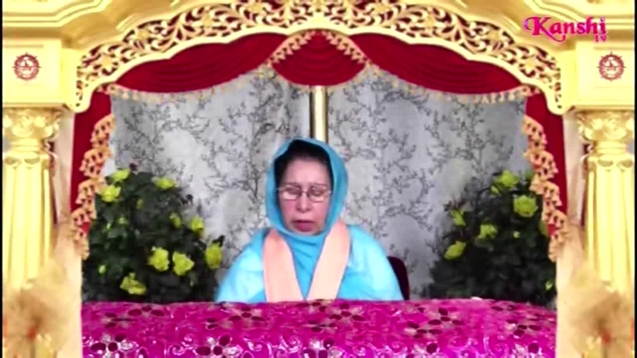 A woman in a blue head covering sits behind a table, speaking into a microphone. The Kanshi TV logo is visible above her, and the background is ornate with gold and red accents.
