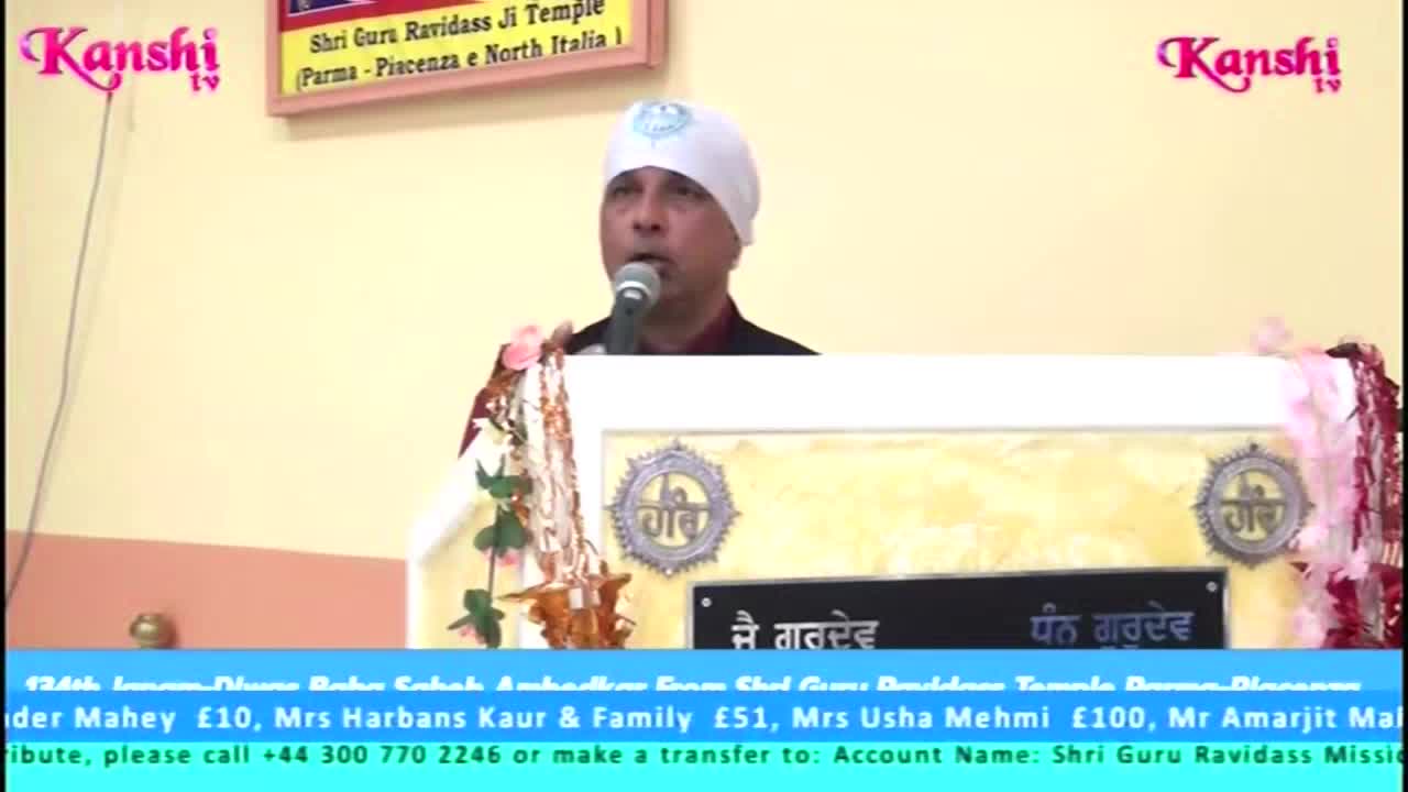 A man in a white turban speaks into a microphone from behind a podium, the Kanshi TV logo visible in the corner. Below, a list of donors and contact information scrolls on a blue banner.
