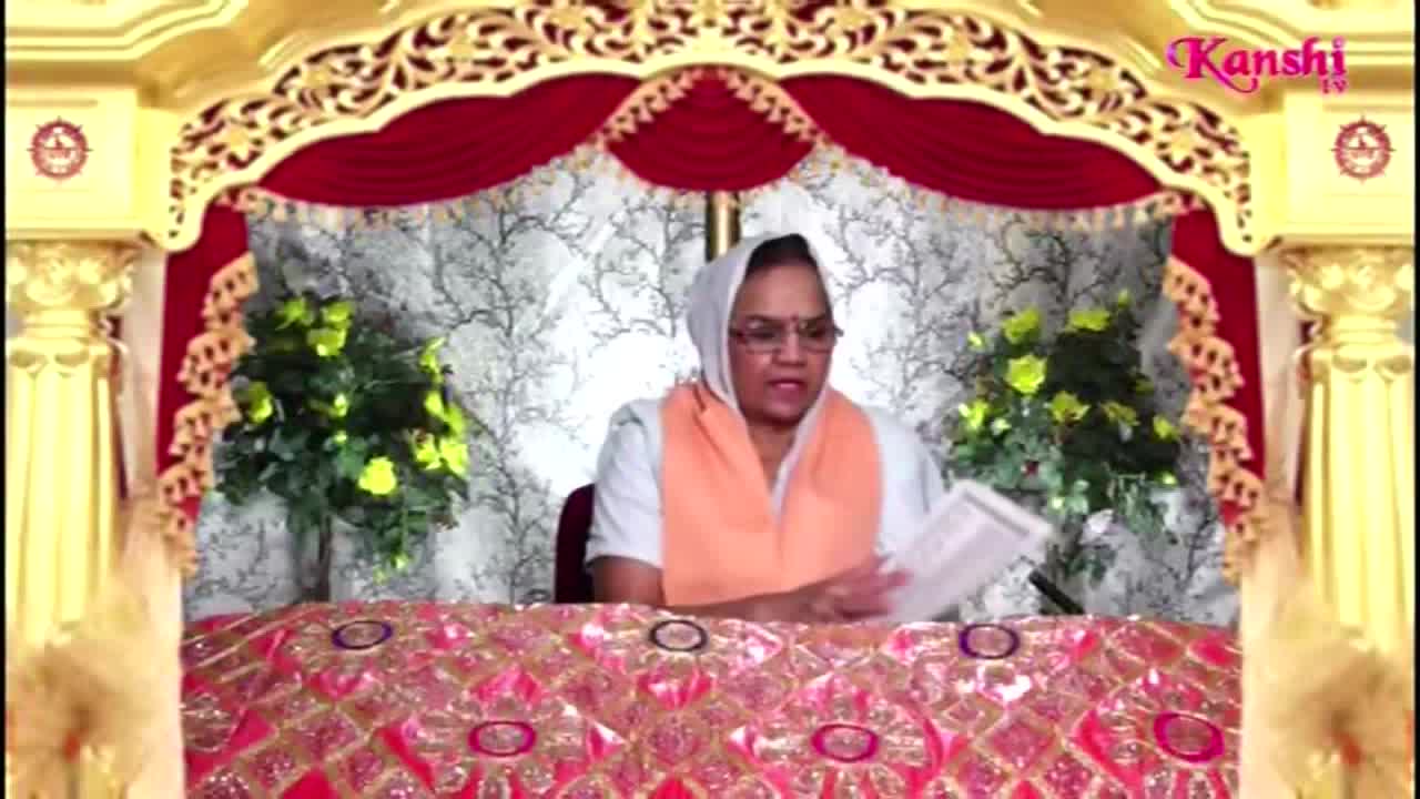A woman in a headscarf and glasses is holding a paper, speaking from behind a decorated table. The Kanshi TV logo is visible in the upper right corner, and the background is ornate.
