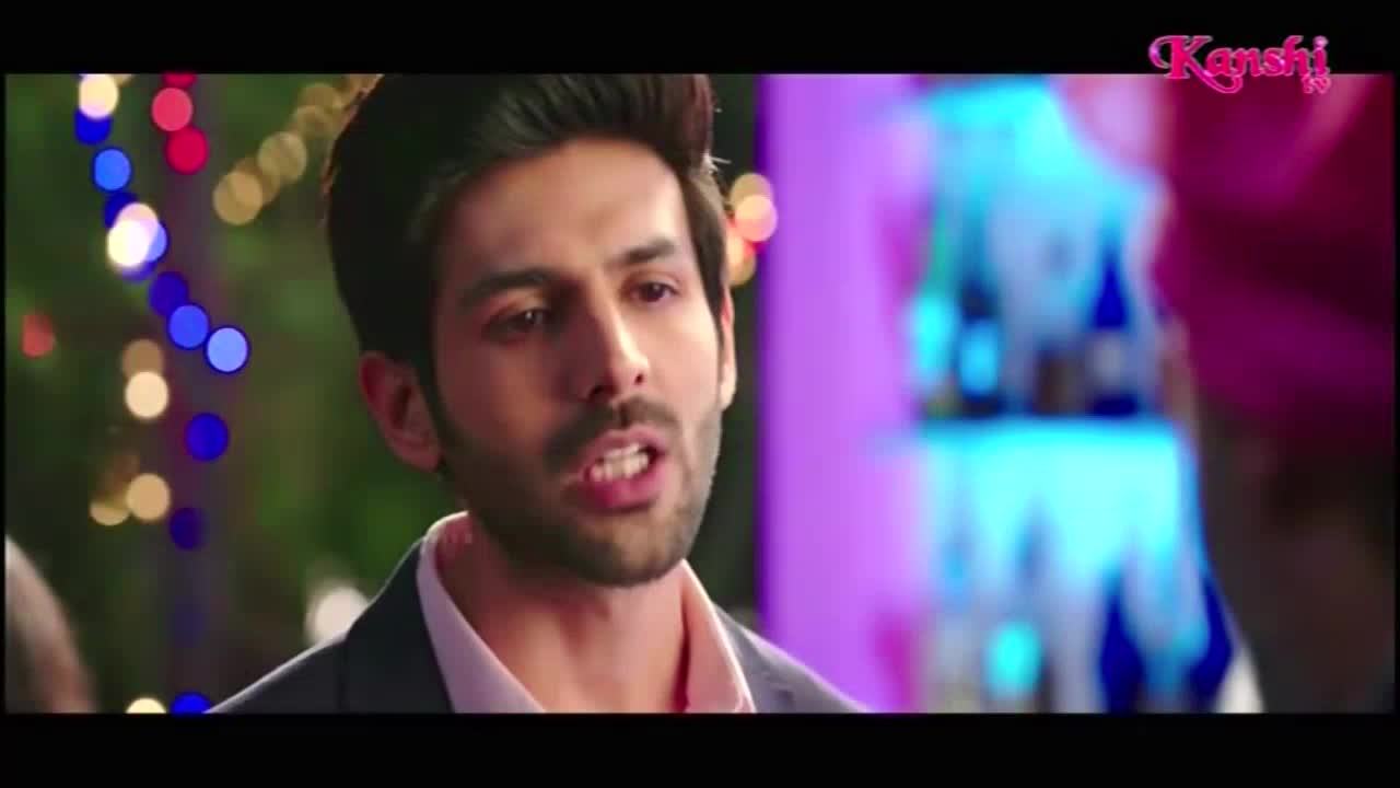 A man in a suit jacket is speaking, his mouth open in mid-sentence. Behind him, colorful lights and a blurred bar scene are visible, all under the Kanshi TV logo.
