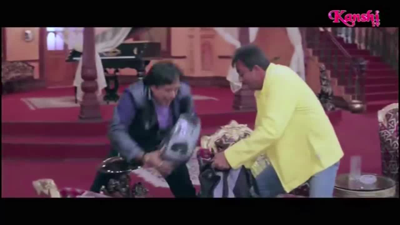 A man in a blue vest swings a helmet, while another in a yellow jacket reaches into a pile of clothes. The scene is playing on Kanshi TV, with a logo in the corner.

