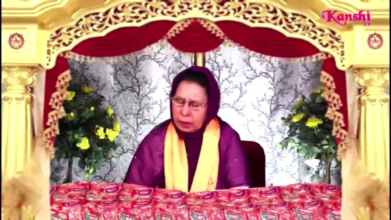 A woman in a purple outfit and glasses sits centered, speaking. The Kanshi TV logo is visible in the upper right corner, and the backdrop is ornately decorated.
