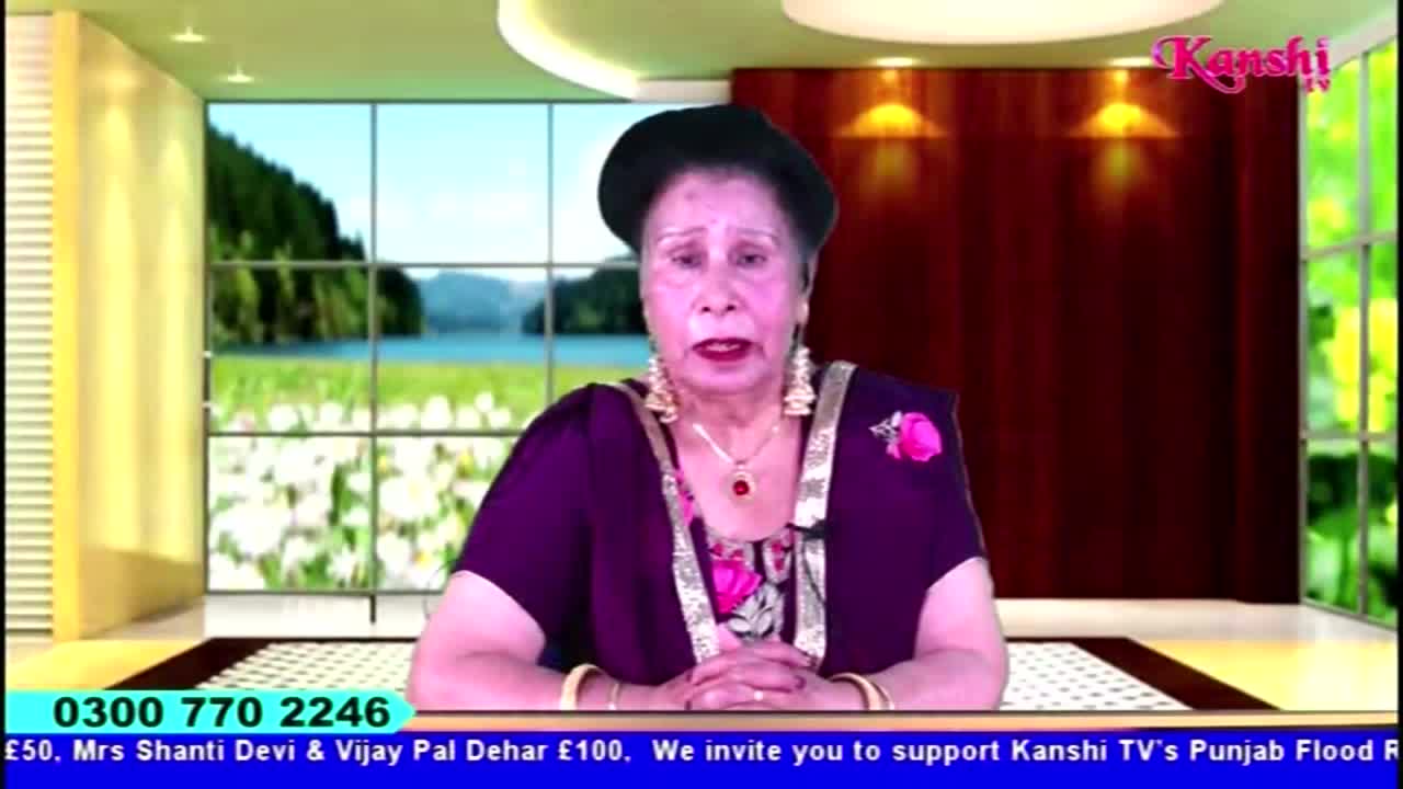 A woman in a dark purple outfit is speaking directly to the camera on Kanshi TV. Behind her, a backdrop shows a landscape with a lake and green trees.
