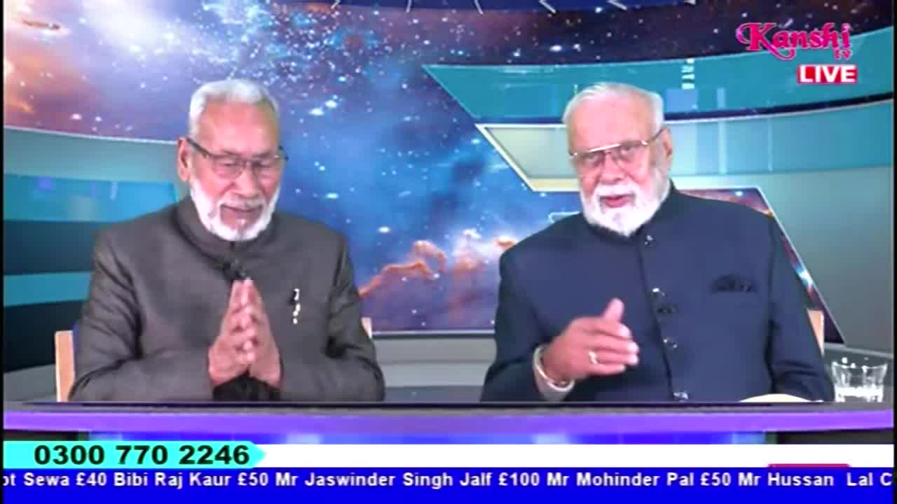 Two men with white beards and glasses sit at a desk, speaking on Kanshi TV. The man on the right gestures with his hand, while the other keeps his hands clasped in front of him.
