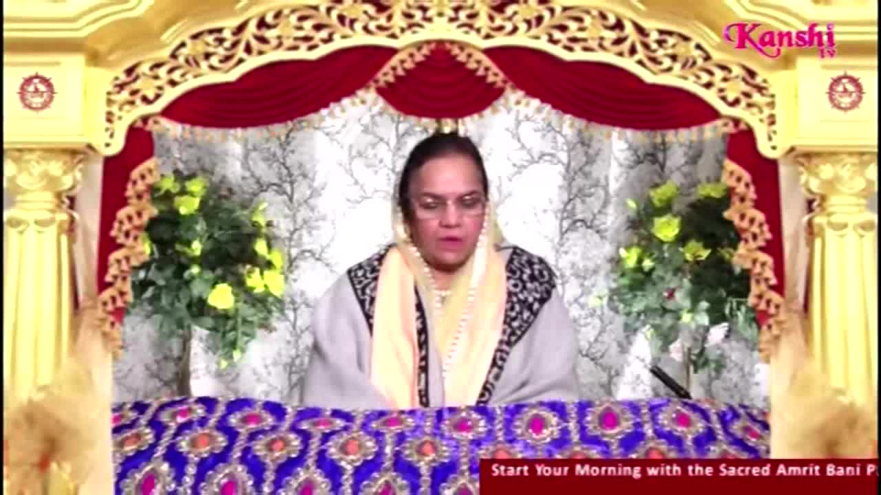 A woman in glasses speaks from behind a table covered in a patterned cloth. The Kanshi TV logo sits in the corner, and the backdrop is ornate with gold and red accents.
