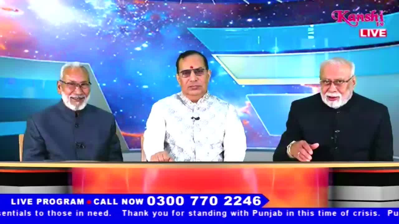 Three men are seated behind a desk, each wearing a dark suit jacket. The Kanshi TV logo is visible in the upper right corner, and a call-in number scrolls at the bottom of the screen.
