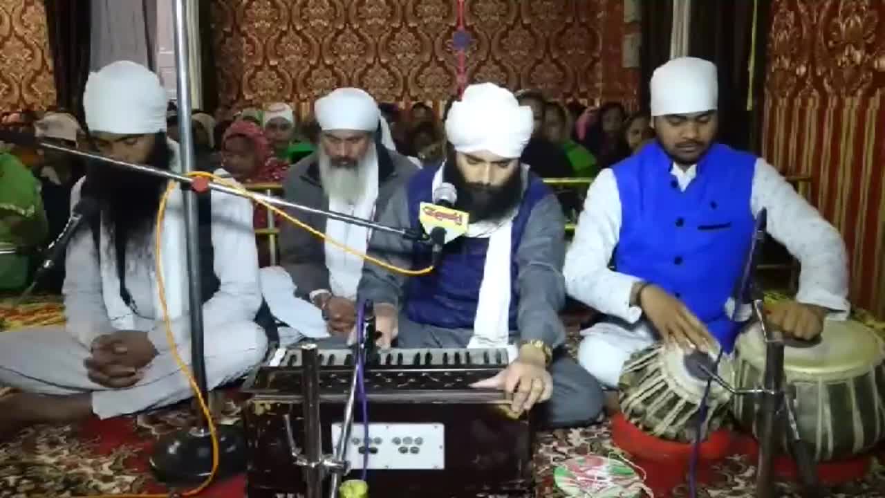 A man in a blue vest strikes the tabla with his hands while another plays the harmonium. The Kanshi TV logo is visible on the microphone in front of the man playing the keyboard.
A man in a blue vest strikes the tabla with his hands while another plays the harmonium. The Kanshi TV logo is visible on the microphone in front of the man playing the keyboard.