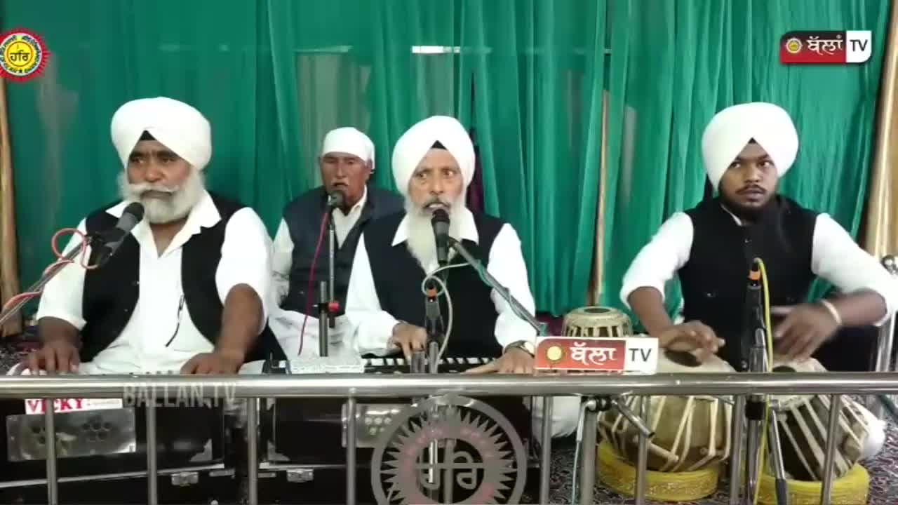 Three men in white turbans and vests sing into microphones, accompanied by a keyboard and a set of tabla drums. The scene is being broadcast by Kanshi TV, with a logo visible in the corner.
Three men in white turbans and vests sing into microphones, accompanied by a keyboard and a set of tabla drums. The scene is being broadcast by Kanshi TV, with a logo visible in the corner.