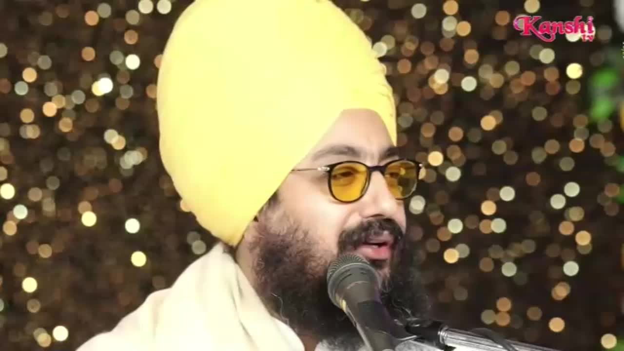 A man with a yellow turban and glasses speaks into a microphone, his face illuminated by the lights. The Kanshi TV logo is visible in the corner.
A man with a yellow turban and glasses speaks into a microphone, his face illuminated by the lights. The Kanshi TV logo is visible in the corner.