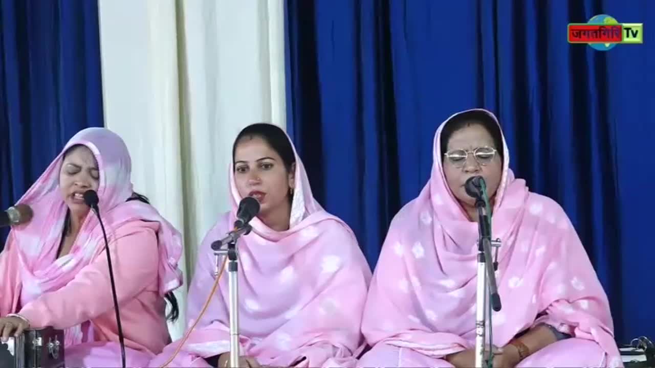 Three women in matching pink outfits stand behind microphones, singing. The Kanshi TV logo is visible in the corner.
Three women in matching pink outfits stand behind microphones, singing. The Kanshi TV logo is visible in the corner.